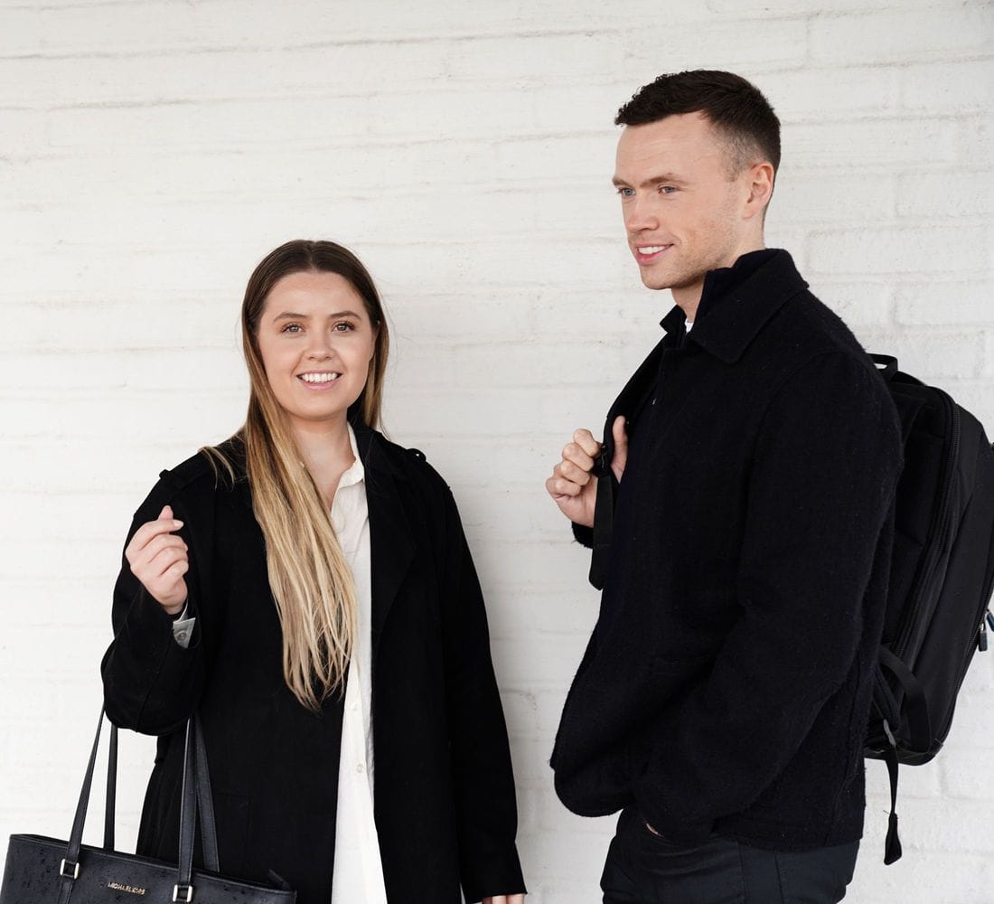 Ung kona og ungur maður standa við hvítan vegg