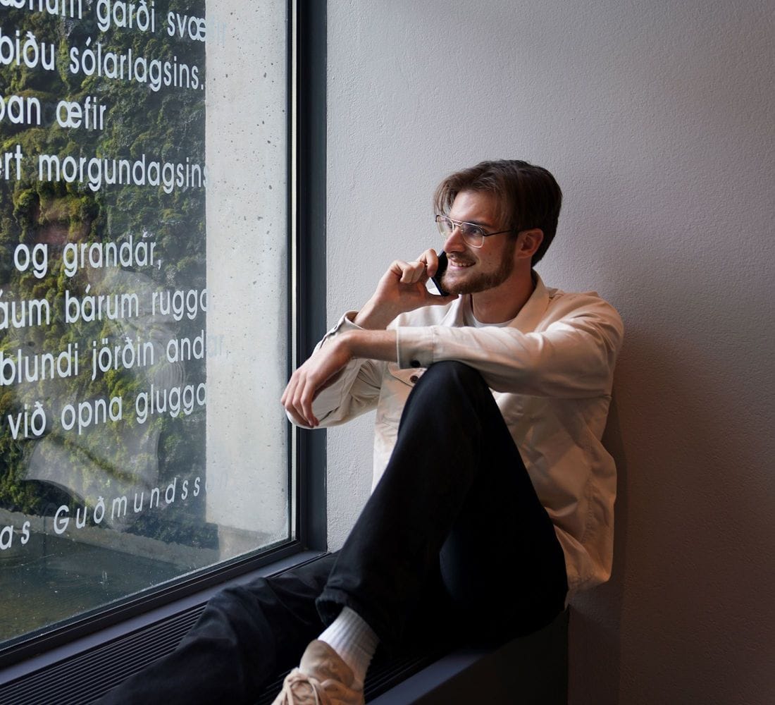 Ungur maður situr í glugga í símanum